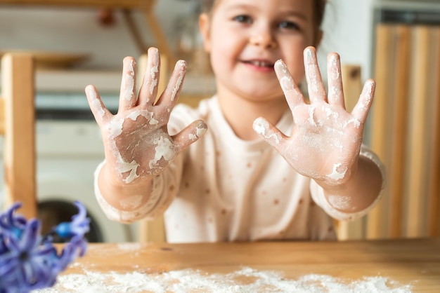 Garota cozinha em casa em uma cozinha brilhante, uma criança agita farinha na mesa, bebê ajuda a mãe e ri