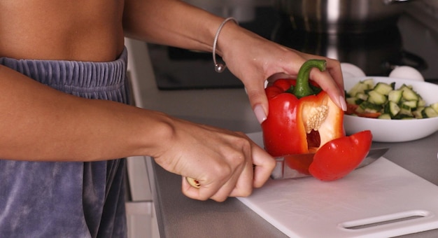 Garota cozinheira na cozinha corta páprica vermelha com legumes com uma faca.