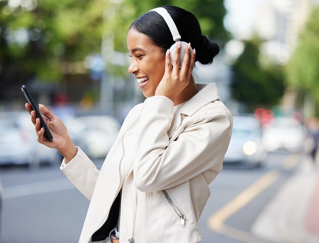 Garota da cidade feliz com telefone e fones de ouvido em videochamada enquanto caminha relaxa na rua para trabalhar ou em casa Mulher negra ou estudante rindo de piada meme ou vídeo online enquanto viaja para um local