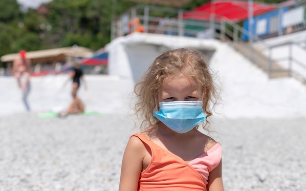 Garota da criança vestindo uma máscara protetora na praia