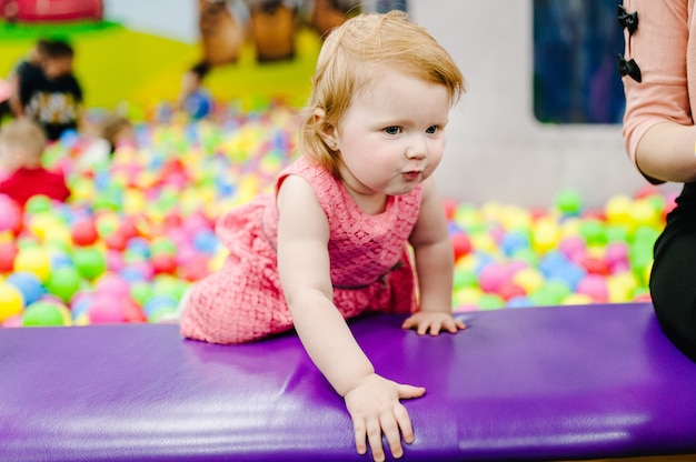 Garota da risada feliz brincando com brinquedos, bolas coloridas no playground, piscina de bolinhas na sala de jogos. Criança bonita se divertindo na piscina na festa de aniversário no parque de diversões de crianças.