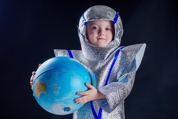 Garota de astronauta de fantasia vestida feliz segurando o globo do mundo em um fundo preto no estúdio