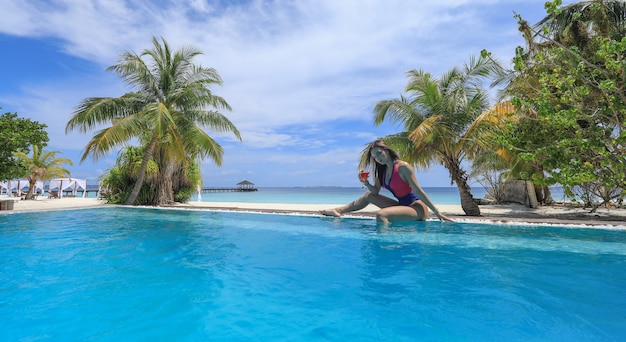 garota de biquíni em uma piscina tropical olhando para o oceano