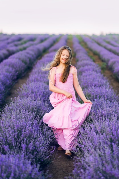 Garota de cabelo comprido em um campo de lavanda Uma garota de vestido rosa longo atravessa um campo com flores