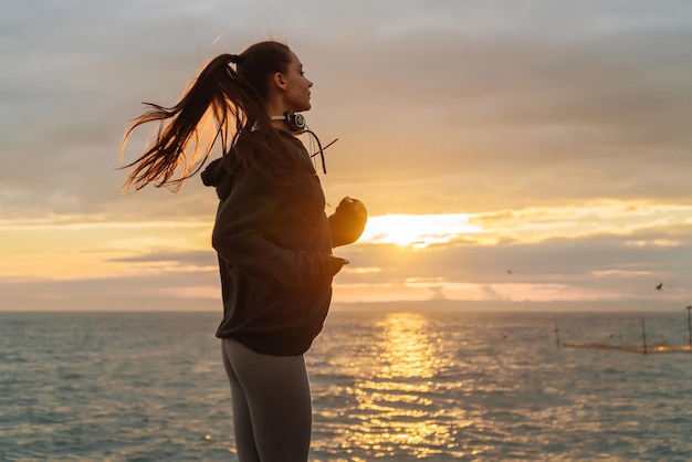 Garota de cabelos compridos esportiva ativa corre ao redor do mar ao pôr do sol quer perder peso