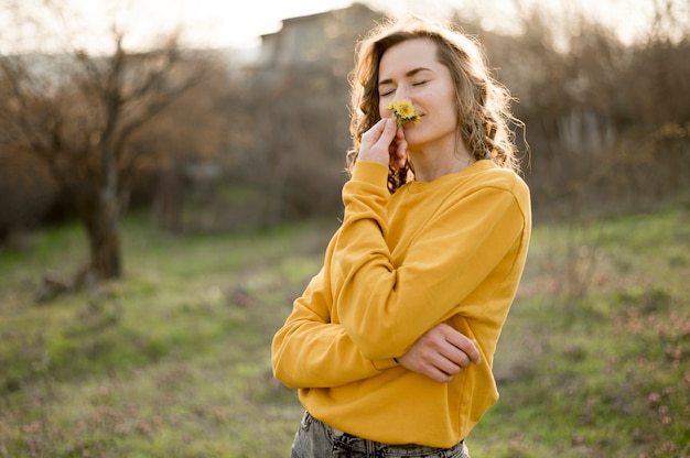 Foto garota de camisa amarela, cheirando uma flor