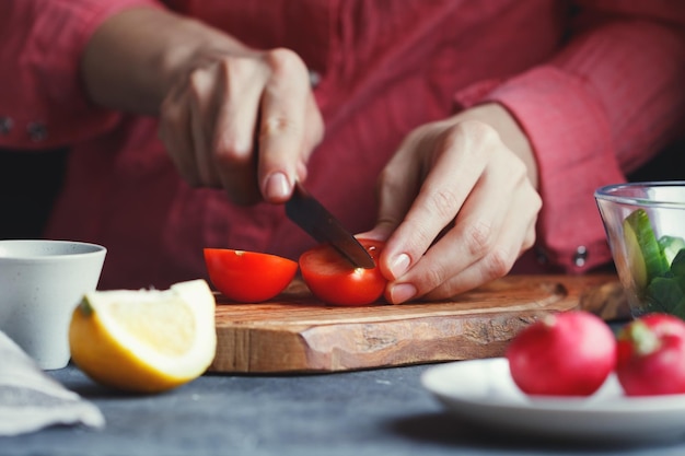 Garota de camisa rosa corta um tomate fresco em uma placa de madeira texturizada cercada por legumes Uma série de fotos sobre a preparação da salada de legumes de verão