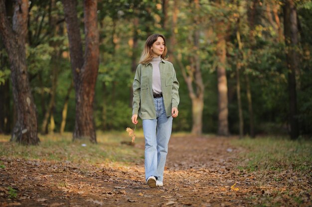 garota de camisa verde e jeans azul na floresta de outono garota segurando uma folha de bordo nas mãos