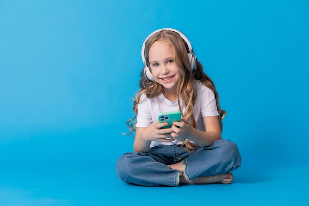 garota de camiseta branca e jeans ouve música através de fones de ouvido em um smartphone enquanto está sentado