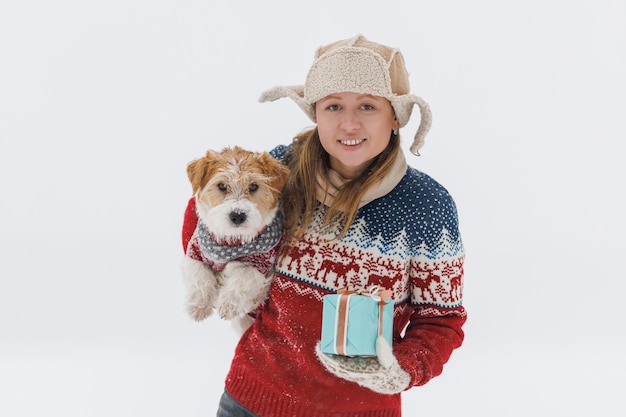 Garota de casaco marrom dá um Jack Russell Terrier um presente em um fundo branco durante uma nevasca O cachorro senta-se nas mãos de um homem Conceito de Natal