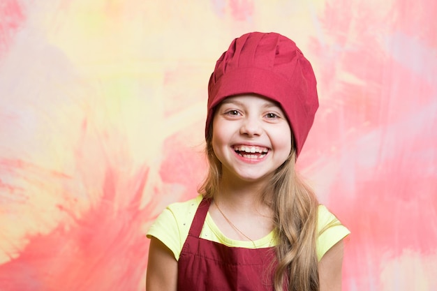 Garota de chapéu de chef e avental. conceito de carreira, uniforme, sonho, ocupação e profissão. criança e infância feliz. cozinhar e brincar. cozinheiro de criança sorrindo na parede colorida.