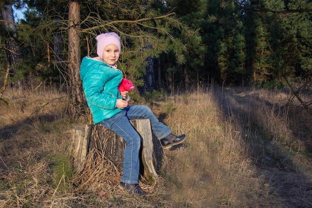 Garota de cinco anos feliz sentada em uma jaqueta em um toco na floresta na primavera