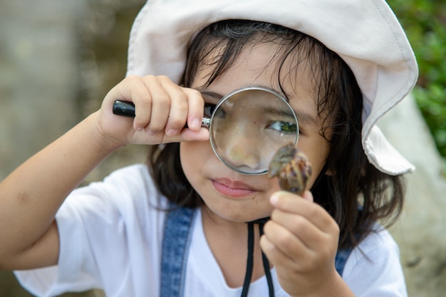 Garota de criança feliz explorando a natureza com uma lupa e um caracol. Ele está se divertindo no jardim. O conceito de criança está pronto para ir para a escola.