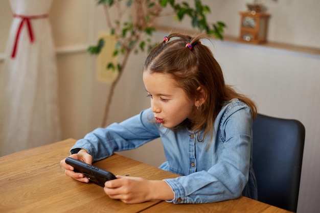 Garota de criança feliz jogando no celular em casa