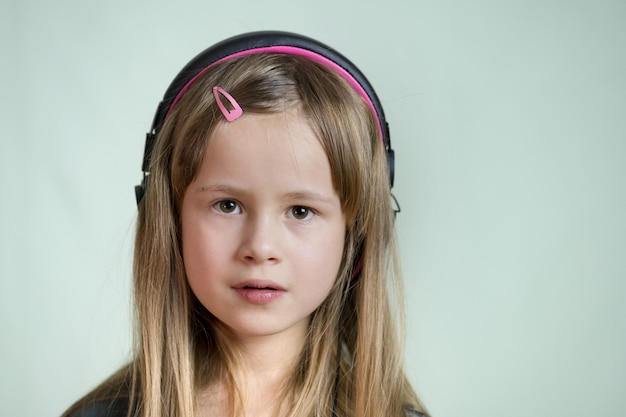 Garota de criança muito sorridente ouvindo música em fones de ouvido rosa grandes.