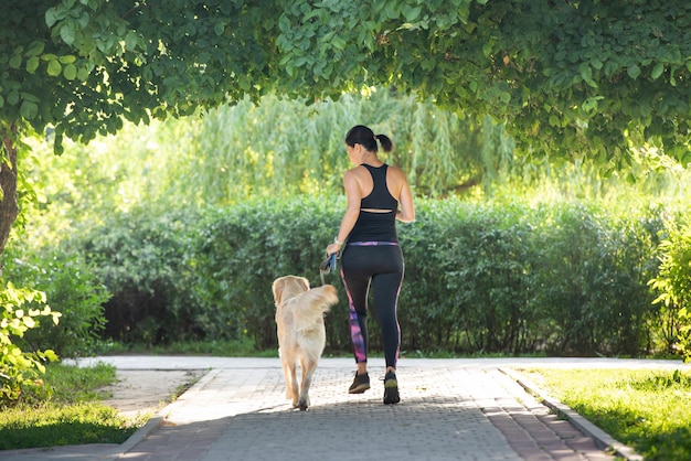 Garota de esporte correndo com cachorro retriever dourado ao ar livre no parque, jovem mulher correndo com cachorro cachorrinho ...