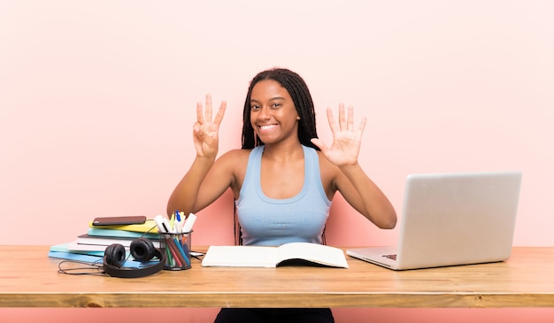 Garota de estudante adolescente americano africano com cabelo longo trançado no seu local de trabalho, contando oito com os dedos