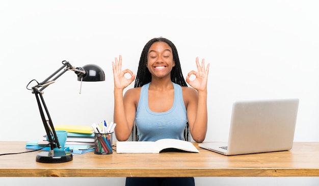 Garota de estudante adolescente americano africano com longos cabelos trançados em seu local de trabalho em pose de zen