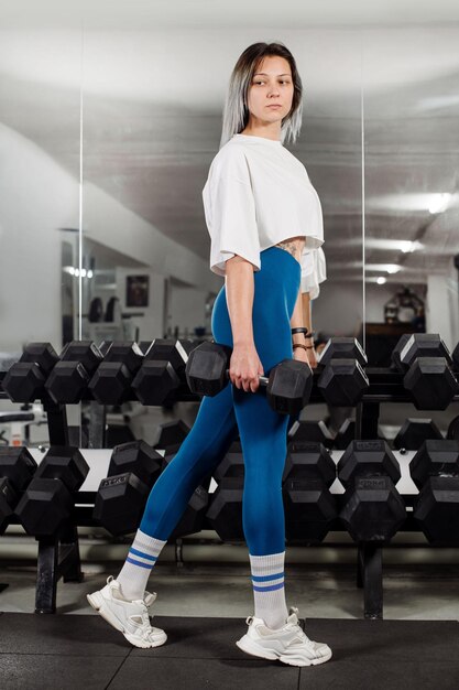 Garota de fitness desportiva está posando para os halteres no ginásio