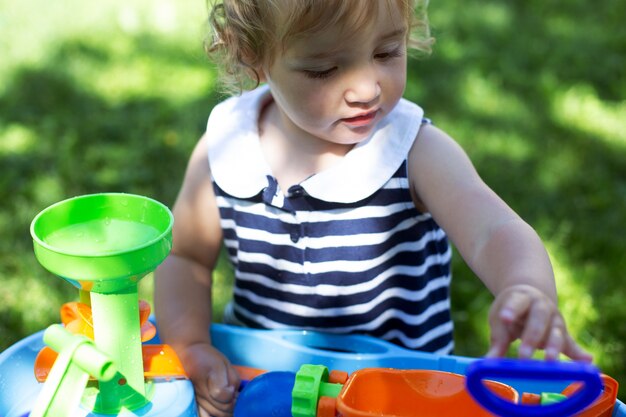 Garota de giro da criança brincando com um brinquedo de água ao ar livre. Dia de sol de verão, bebê usando vestido listrado