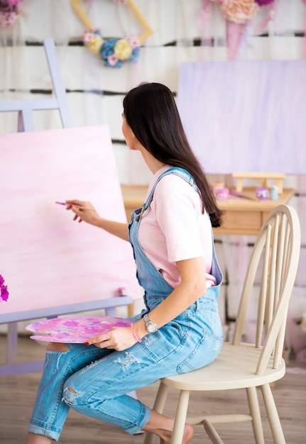 Garota de macacão jeans azul está pintando na sala