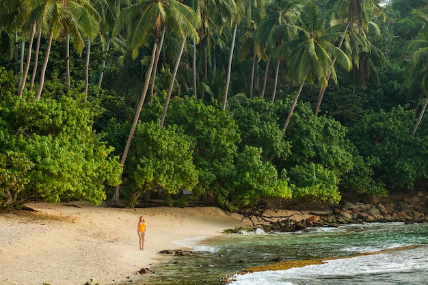 Garota de maiô caminhando em uma praia tropical