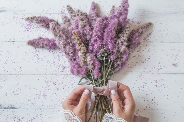 Garota de mãos amarrando um buquê de flores cor de rosa.