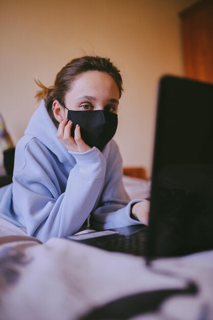 Garota de máscara preta trabalha em um laptop em casa em isolamento em quarentena processamento de fotos vintage