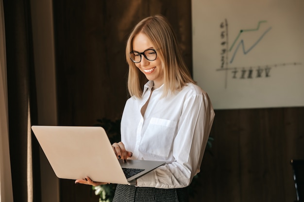 Garota de negócios com um lindo sorriso tem um laptop nas mãos, trabalho de escritório.