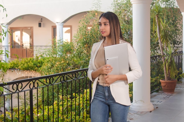 Garota de negócios jovem carregando um laptop com os braços na varanda do hotel