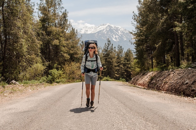 Garota de óculos de sol caminhando na estrada com mochila caminhadas e bastões de caminhadas