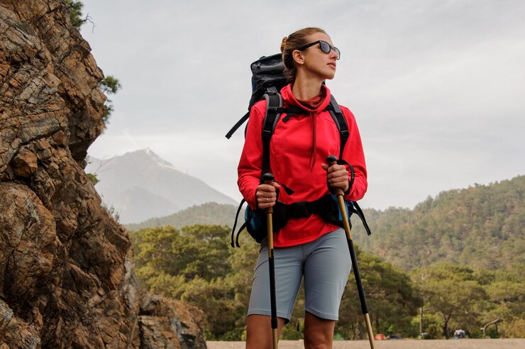 Garota de óculos de sol em pé nas rochas com caminhadas mochila e bengalas