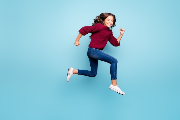 Garota de perfil lateral de corpo inteiro correndo sobre uma parede azul