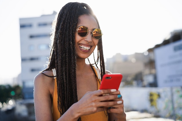 Garota de raça mista boêmia usando smartphone ao ar livre com a cidade ao fundo - Tecnologia e conceito de estilo de vida moderno - Foco no rosto