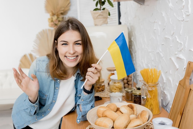 Garota de sorte olha para a câmera com a bandeira da Ucrânia em sua cozinha