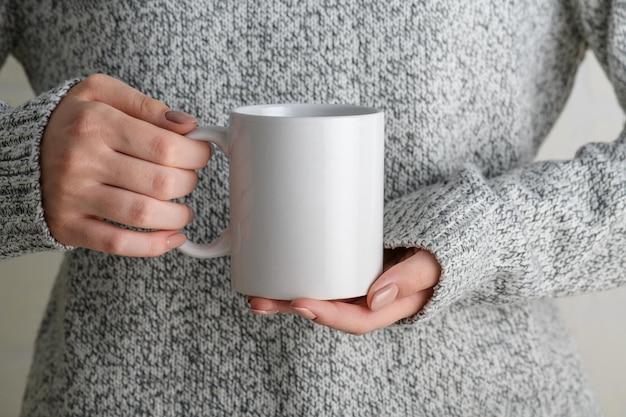 Garota de suéter cinza segurando caneca de café de porcelana branca simulada de perto