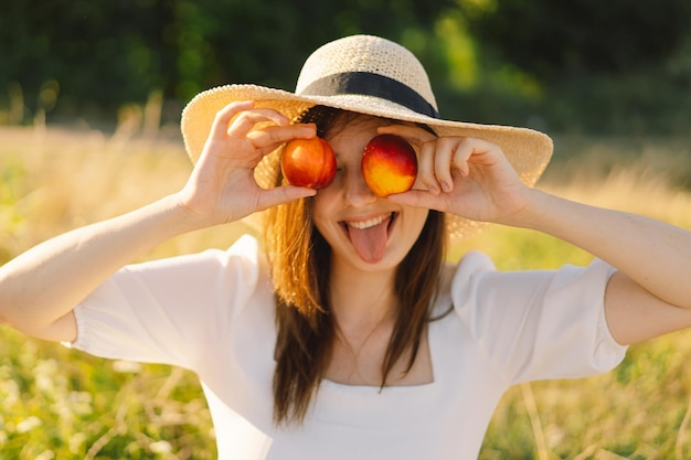 Garota de verão feliz e despreocupada em campo ao ar livre com frutas de pêssego laranja jovem come pêssego cenário de piquenique de verão