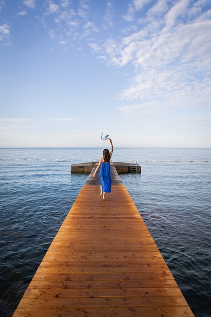 Foto garota de vestido azul corre em um píer de madeira perto do mar. montenegro, budva