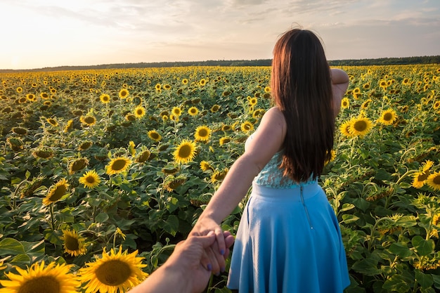 Garota de vestido azul sai no campo de girassóis no pôr do sol Siga-me o conceito