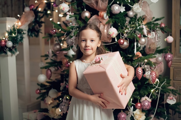 Garota de vestido em pé perto da árvore de Natal e segurando presentes