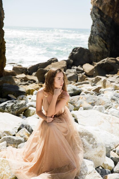 Garota de vestido longo perto de rochas e oceano