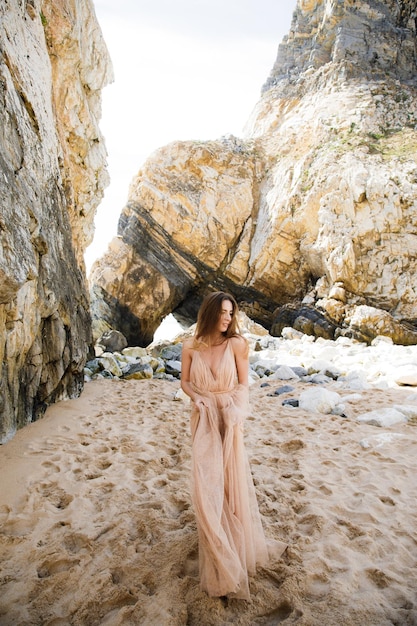 Garota de vestido longo perto de rochas e oceano