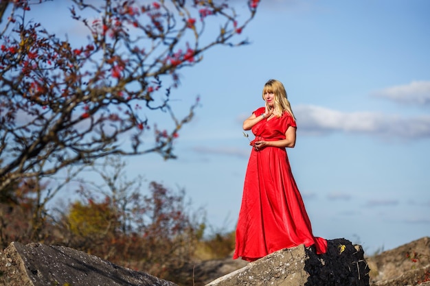 Garota de vestido vermelho na rocha ou estrutura arruinada de concreto com Rowan no fundo do outono