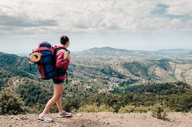 Garota de viagem jovem com mochila caminha no fundo da bela paisagem mar e colinas de Afrodite Chipre destino popular para férias de verão