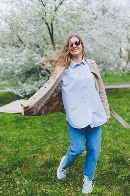 Garota de vista traseira andando sob macieira florescendo no parque natural na encosta da colina em Praga Jovem elegante de chapéu e casaco marrom desfrutando de jardim florido no dia ensolarado de primavera