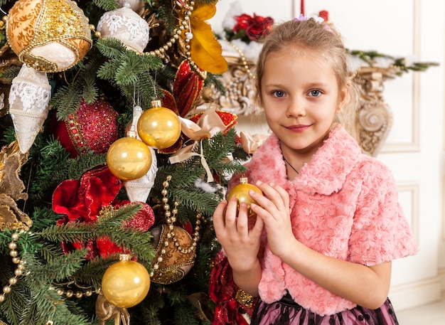 Garota decora uma árvore de natal, uma garota de natal segurando um brinquedo nas mãos de