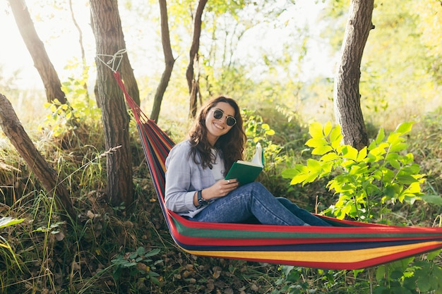 garota descansando no parque com um livro na rede