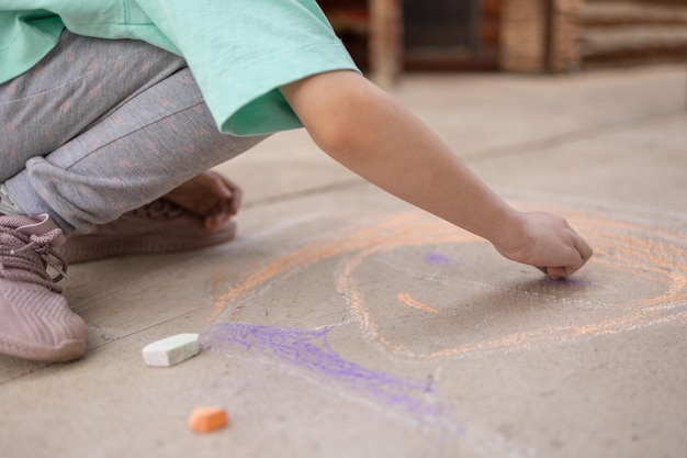 Garota desenha com giz de cera colorido no pavimento Desenhos infantis com giz na parede Criança criativa Alegria da infância