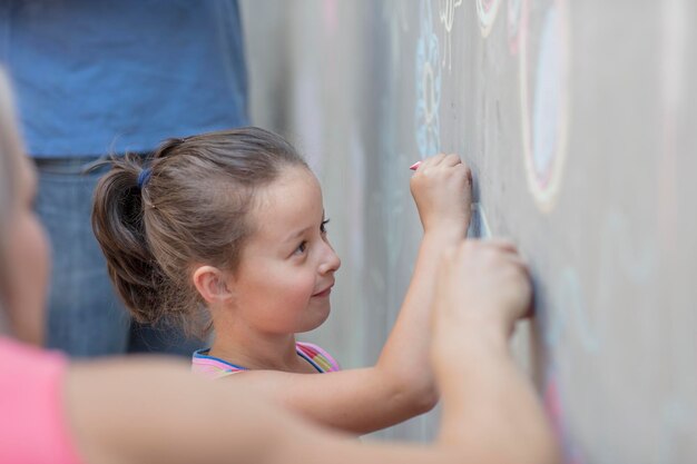 Garota desenhando fotos coloridas com giz em uma parede de concreto