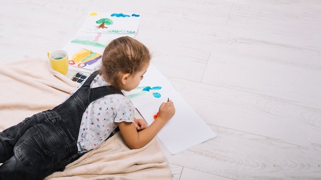 Garota desenhando por cores de água no papel e deitado no chão